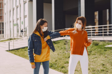 COVID Young women in medical masks greeting each other on city street