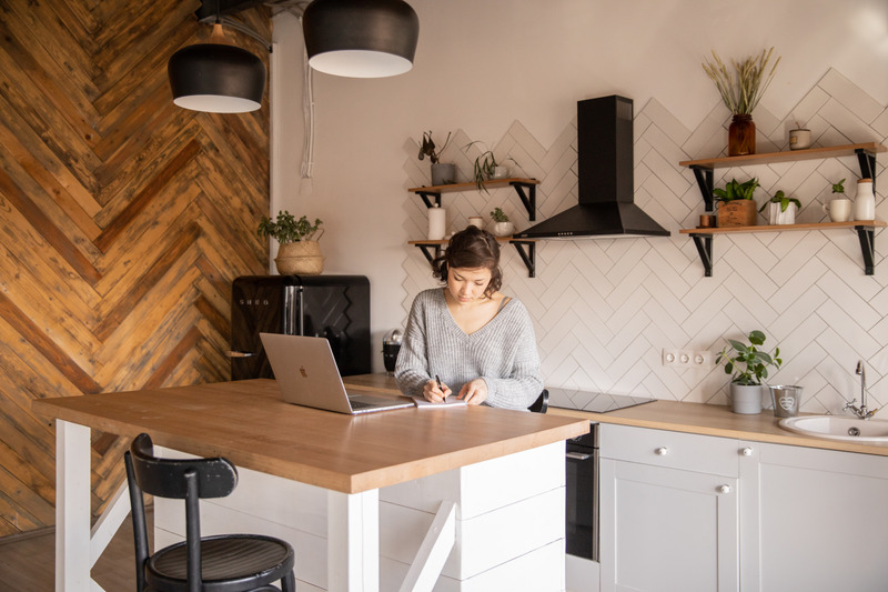 Canva - Busy female freelancer with laptop taking notes in kitchen