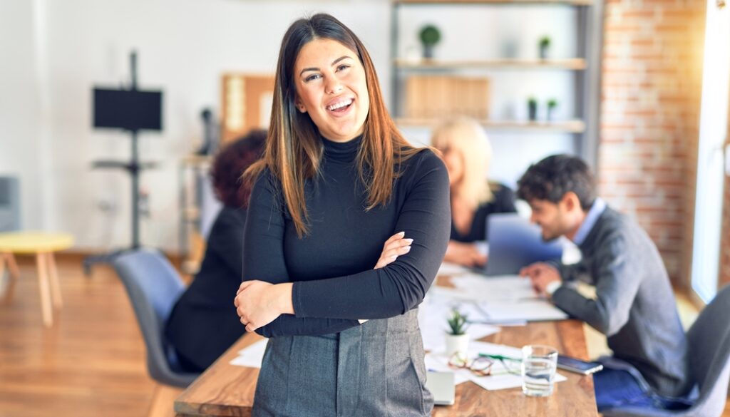 Group of business workers working together. Young beautiful woman standing smiling happy looking at the camera at the office