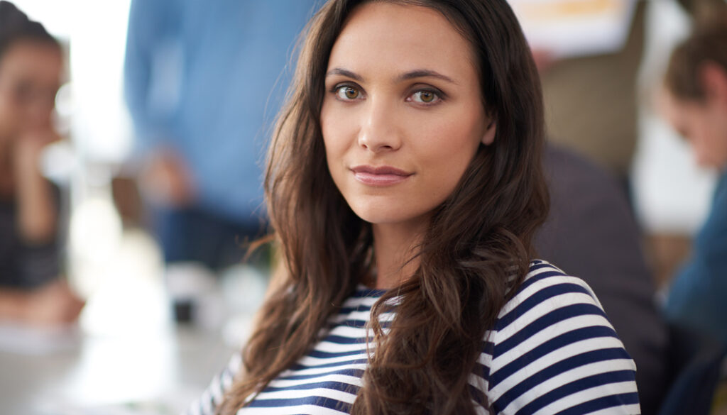 Her work stands out from the crowd. Portrait of an attractive young woman sitting in an office with colleagues in the background.