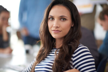 Her work stands out from the crowd. Portrait of an attractive young woman sitting in an office with colleagues in the background.