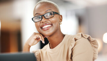 Black woman, thinking and smile, relax at desk with laptop for content creation ideas at digital marketing startup. Copywriter, happy female and contemplating with inspiration for copywriting job