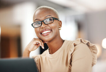 Black woman, thinking and smile, relax at desk with laptop for content creation ideas at digital marketing startup. Copywriter, happy female and contemplating with inspiration for copywriting job