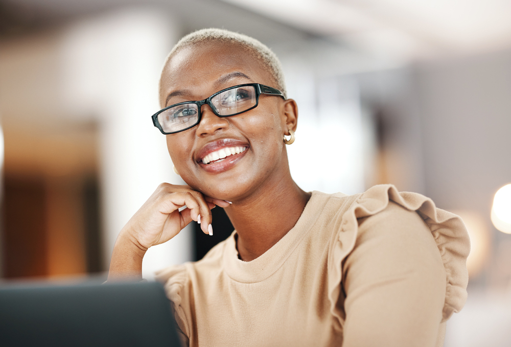 Black woman, thinking and smile, relax at desk with laptop for content creation ideas at digital marketing startup. Copywriter, happy female and contemplating with inspiration for copywriting job