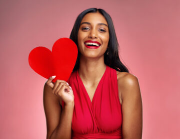 Portrait, heart and social media with a woman on a pink background in studio for love or romance. Smile, emoji and valentines day with a happy young female holding a shape or symbol of affection