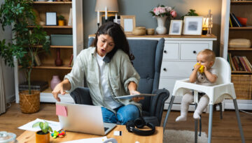 Mother working on laptop and talking on computer webcam video call communication with business partners while baby playing. Woman work from home and caring for kids.