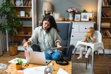 Mother working on laptop and talking on computer webcam video call communication with business partners while baby playing. Woman work from home and caring for kids.