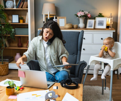 Mother working on laptop and talking on computer webcam video call communication with business partners while baby playing. Woman work from home and caring for kids.