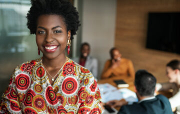 close up of beautiful young smiling professional black african business woman, coworkers hold a meeting in background