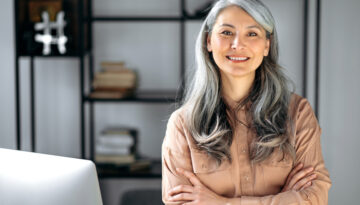 Portrait of a successful confident mature gray-haired lady, business woman, ceo or business tutor, standing in the office with arms crossed, looking and friendly smiling into the camera