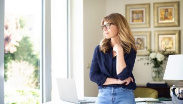 Attractive smiling mature woman standing at desk and thinking