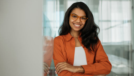 Smiling African American business woman wearing stylish eyeglasses looking at camera standing in modern office. Successful business and career concept
