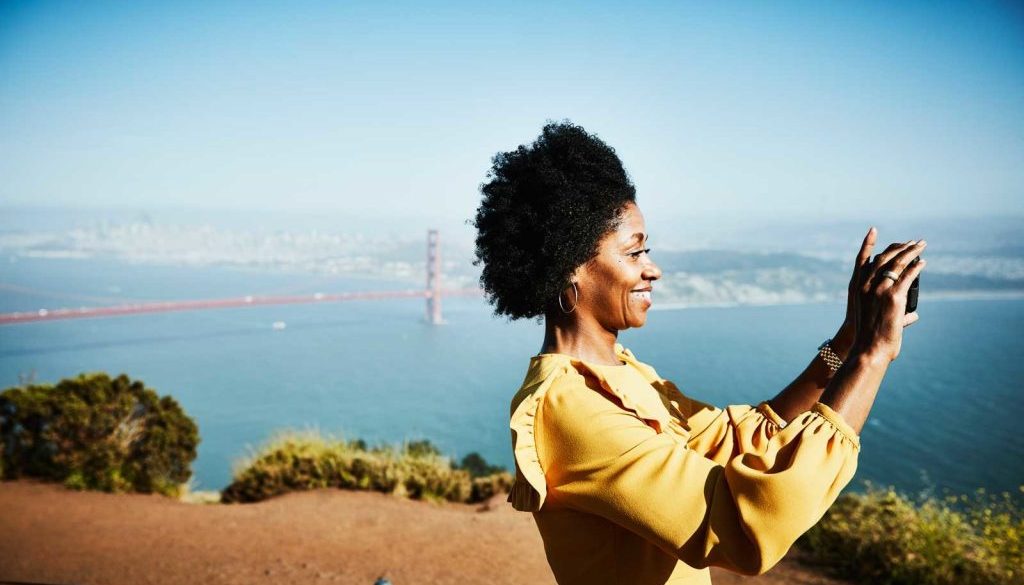 Smiling woman taking photo with smartphone while standing at vista above San Francisco