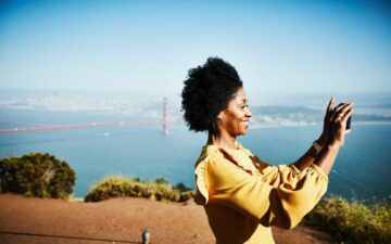 Smiling woman taking photo with smartphone while standing at vista above San Francisco