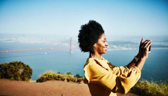 Smiling woman taking photo with smartphone while standing at vista above San Francisco